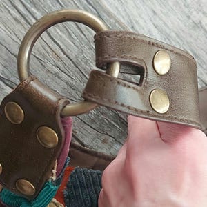 May include: A brown leather strap with a metal ring and brass accents. The strap is attached to a patchwork bag made of different fabrics, including corduroy and denim.