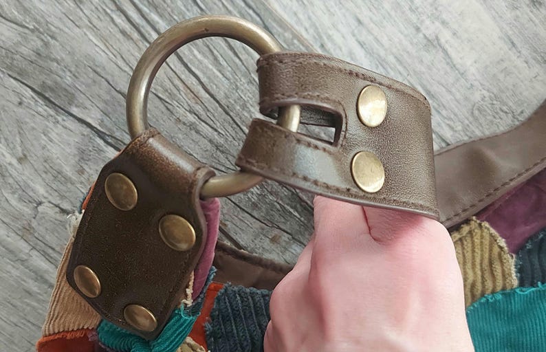 May include: A brown leather strap with a metal ring and brass accents. The strap is attached to a patchwork bag made of different fabrics, including corduroy and denim.