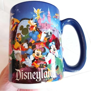 May include: A blue ceramic Disneyland Resort mug featuring various Disney characters, including Mickey and Minnie Mouse, Goofy, and Donald Duck. The mug has a dark blue handle and the Disneyland Resort logo.