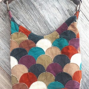 May include: A patchwork shoulder bag made of corduroy fabric in various colors, including teal, brown, red, white, and purple. The bag features a unique design of overlapping semi-circles.