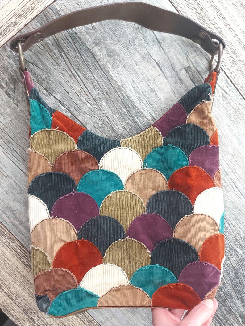 May include: A patchwork shoulder bag made of corduroy fabric in various colors, including teal, brown, red, white, and purple. The bag features a unique design of overlapping semi-circles.