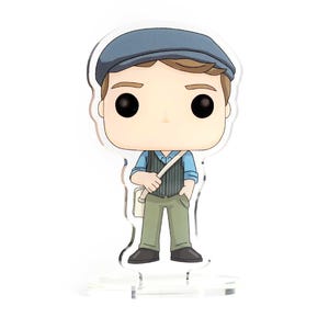 May include: A blue and white figurine of a person wearing a blue cap, a blue shirt, a brown vest, and brown pants. The figurine is holding a white bag over their shoulder.