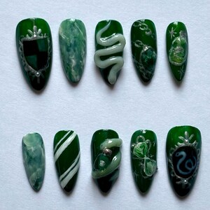 Può includere: Dieci punte per unghie verdi e bianche con diversi design. Alcuni design includono un serpente, una bottiglia di pozione e uno stemma con un serpente.