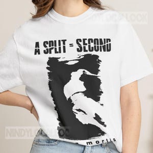 May include: A white short-sleeved t-shirt featuring a black graphic print. The text A SPLIT = SECOND is printed in a bold, distressed font above a black rectangular block containing a white abstract silhouette of a figure in motion.