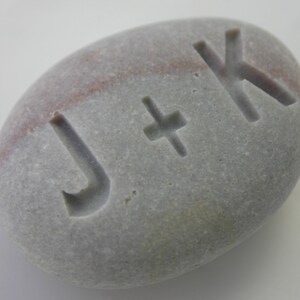 May include: A gray and pink stone with the letters J + K carved into it.