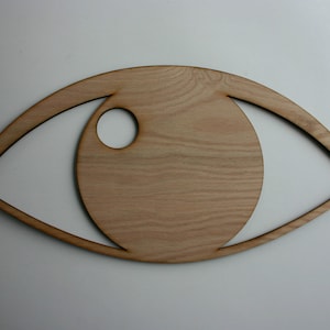 May include: A wooden eye-shaped cutout with a circular hole in the center. The cutout is made of light brown wood with a natural grain pattern.
