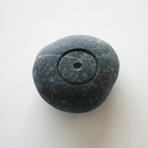 May include: A smooth, dark gray stone with a carved circle and a small hole in the center.