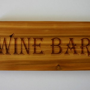 Peut inclure: Une enseigne en bois avec les mots "WINE BAR" gravés dans une police décorative.