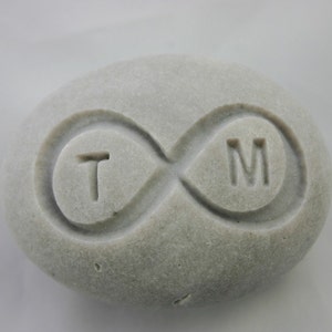 May include: A gray stone with the letters "T" and "M" carved into it, connected by an infinity symbol.