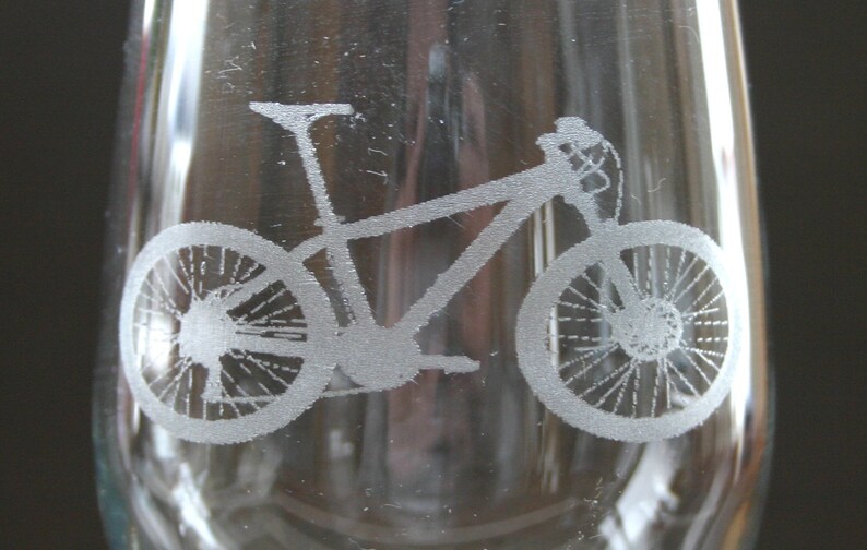 Pu&ograve; includere: Un bicchiere di vetro trasparente con un design inciso di una mountain bike. La bicicletta &egrave; rivolta a destra e ha due ruote, un manubrio e un telaio.