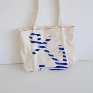 May include: A white canvas tote bag with rope handles. The bag features a blue and white striped anchor design.