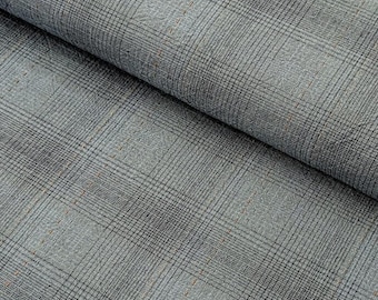 May include: Close-up of a folded fabric with a gray and black plaid pattern. The fabric has a textured appearance with small flecks of orange and brown. The plaid design is a classic pattern, suitable for various apparel and home decor projects.