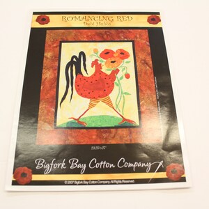 Puede incluir: Una impresión titulada "Romancing Red" de Debt Hubbs, con un gallo rojo estilizado sosteniendo flores. La obra de arte está enmarcada con un borde negro e incluye el texto "Bigfork Bay Cotton Company". La impresión mide 54 x 64 cm.