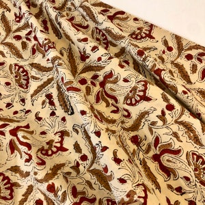 May include: A cream-coloured fabric with a repeating pattern of brown and red floral designs. The fabric is soft and has a subtle sheen.