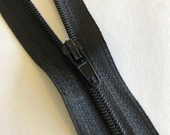 May include: A black zipper with a black slider. The zipper is closed and the slider is in the centre of the zipper.