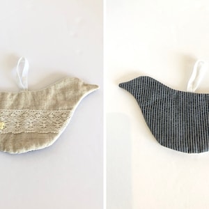 May include: Two fabric bird ornaments. One is beige with lace trim and yellow flower buttons. The other is dark blue with white stripes.