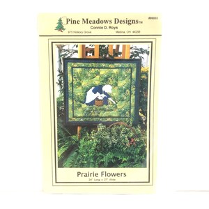 May include: A quilting pattern for a quilt titled "Prairie Flowers" featuring a woman in a blue dress and white apron holding a basket of flowers. The quilt is 24 inches long and 27 inches wide.