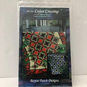 Peut inclure: Un paquet de patron de quilt intitulé "Cajun Crossing" par Bayou Patch Designs. Le motif présente un quilt avec des motifs de losanges rouges, noirs et verts. Les dimensions sont de 160 cm x 193 cm en pointe et de 145 cm x 190 cm en ligne droite.