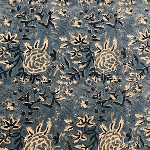 Pode incluir: Um tecido com padrão floral azul e branco. O design apresenta grandes rosas estilizadas e grupos de flores menores, com caules e folhas azuis escuros. O fundo é azul suave, criando uma estética vintage.