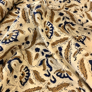 May include: A cream-colored fabric with a blue and brown floral pattern. The fabric has a paisley design and is perfect for crafting or sewing projects.