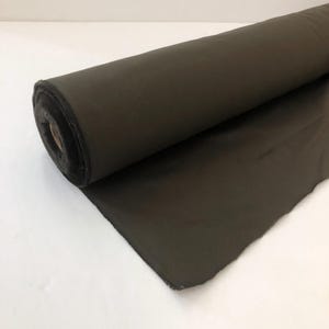 Puede incluir: Un rollo de tela verde oscuro. La tela está enrollada y el extremo está doblado.