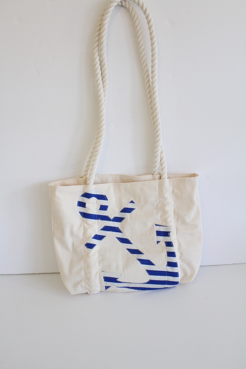 May include: A white canvas tote bag with rope handles. The bag features a blue and white striped anchor design.