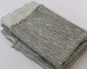 May include: A folded piece of white fabric with a black speckled pattern. The fabric has a raw edge.