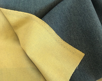 May include: Close-up of a folded piece of fabric. The top layer is a dark denim blue, while the underside is a light tan color. The fabric has a textured appearance, with visible diagonal lines. The edges are neatly finished.