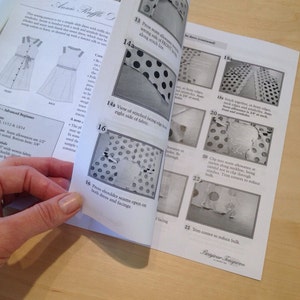 May include: A close-up of a sewing pattern instruction booklet for a dress with a polka dot pattern. The instructions include steps for pressing seams, stitching together fabric pieces, and trimming corners to reduce bulk.