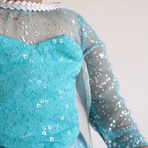 May include: A blue and silver dress with sequins and a sheer overlay. The dress has a sweetheart neckline and long sleeves.