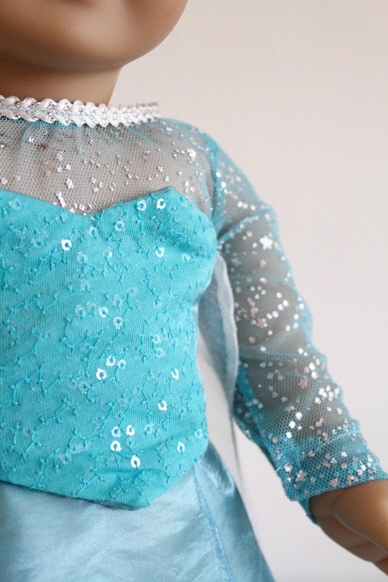 May include: A blue and silver dress with sequins and a sheer overlay. The dress has a sweetheart neckline and long sleeves.