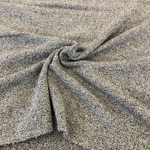 Puede incluir: Primer plano de una tela texturizada gris y blanca con un tacto suave y peludo. La tela está doblada y drapeada, mostrando su textura y caída.