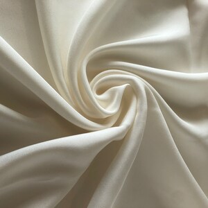 May include: A close-up of a smooth, ivory-colored fabric with soft, flowing folds.