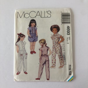 May include: McCall's sewing pattern number 4693 for a child's jumpsuit. The pattern includes three different styles: a white jumpsuit with lace trim, a striped jumpsuit, and a floral jumpsuit. The pattern is for size 2.