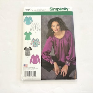 May include: Simplicity sewing pattern number 1315 for a blouse with a gathered neckline. The pattern includes five different views of the blouse, including a purple blouse with long sleeves and a gathered neckline, a green blouse with short sleeves, and a floral blouse with short sleeves. The pattern is designed for sizes 8-14.
