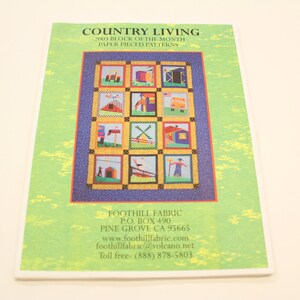 May include: A green and white paper booklet with the title "COUNTRY LIVING 2003 BLOCK OF THE MONTH PAPER PIECED PATTERNS". The cover features a colourful quilt block design with a variety of houses and other country-themed images. The booklet also includes contact information for Foothill Fabric, including their website and toll-free number.