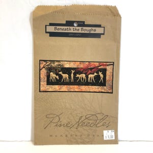 May include: A brown paper bag with a printed image of a quilt pattern featuring a row of white deer under a tree with red leaves. The text on the bag reads "Beneath the Boughs" and "Pine Needles McKenna Ryan 4.04 $9.00".