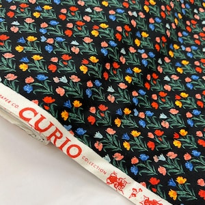 Pode incluir: Tecido preto com um padrão repetitivo de tulipas coloridas. O tecido tem uma etiqueta branca com o texto "CURIO COLLECTION" em vermelho.