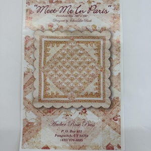 May include: A printed pattern for a quilt titled "Meet Me In Paris." The design features a floral pattern in shades of pink, cream, and gold. The finished size is 100" x 100". The designer is Johná Lee Burk. The pattern is from Amber Rose Press.