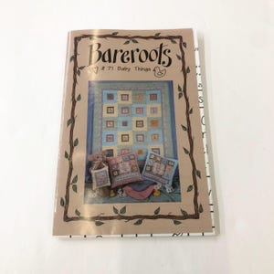 Puede incluir: Un libro titulado "BareRoots" con un corazón y el número 71. El libro presenta una colcha para bebé con un diseño de patchwork azul y amarillo. La colcha está rodeada por un borde de vid marrón con hojas verdes.