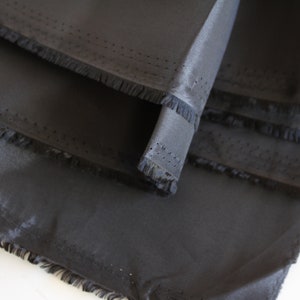 May include: Close-up of black fabric with a fringed edge. The fabric is folded in layers, showing the texture and sheen.