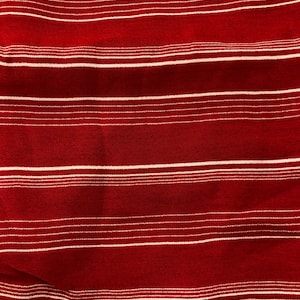 May include: Close-up of a red fabric with horizontal white stripes. The stripes are evenly spaced across the material, creating a textured pattern. The fabric appears to be soft and possibly woven.