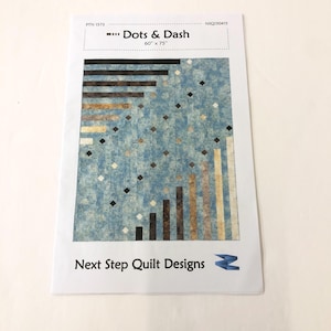 May include: A quilt pattern for a quilt called "Dots & Dash" by Next Step Quilt Designs. The pattern is for a 60 inch by 75 inch quilt. The pattern features a geometric design with black, brown, tan, and white squares and rectangles on a blue background.