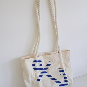 May include: A white canvas tote bag with rope handles and a blue and white striped anchor design.