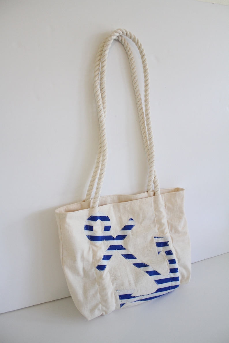 May include: A white canvas tote bag with rope handles and a blue and white striped anchor design.