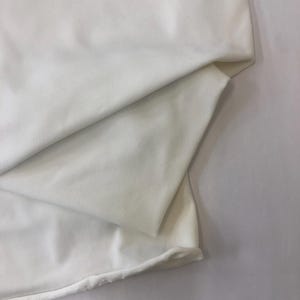 May include: A folded piece of white fabric, possibly cotton or linen, with soft folds and a slightly textured surface. The fabric is a solid, bright white color, and the edges are visible.