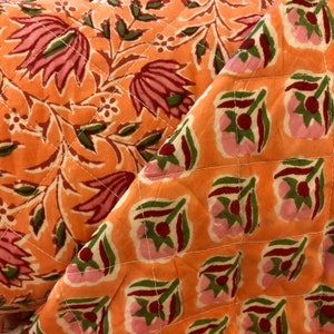 Puede incluir: Primer plano de una tela acolchada con un patrón floral en tonos rosa, verde y naranja. La tela está doblada por la mitad, revelando el patrón en ambos lados.