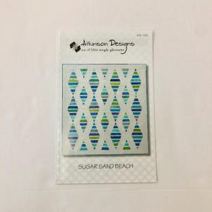 Könnte beinhalten: Ein Quiltmuster für einen Quilt namens "Sugar Sand Beach". Das Muster zeigt einen weißen Hintergrund mit einem sich wiederholenden Muster aus blauen, grünen und weißen Diamanten.