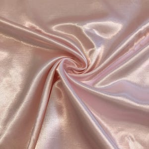 May include: A close-up of a swirl of light pink satin fabric. The fabric has a lustrous sheen and is gathered in a spiral pattern, creating highlights and shadows. The material appears soft and flowing, with subtle texture visible.