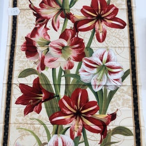 May include: A rectangular fabric panel featuring a botanical print of red and white amaryllis flowers with green stems and leaves. The background is cream with gold swirling lines and snowflake patterns, framed by a black border with gold stars.
